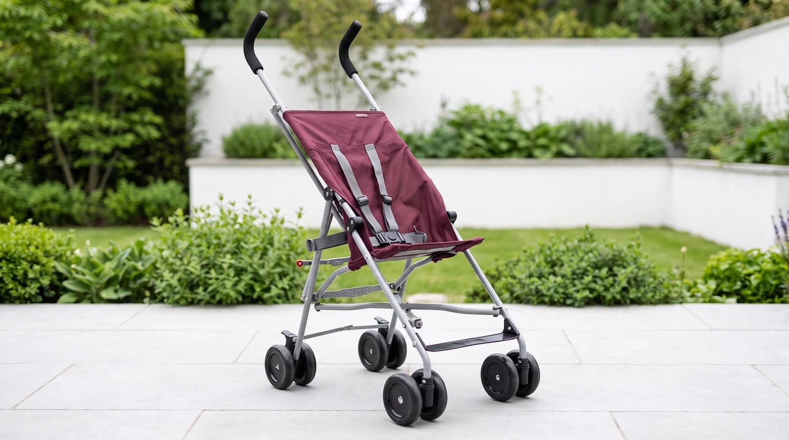 A lightweight, burgundy-coloured buggy with a silver frame, standing empty on a garden patio.
