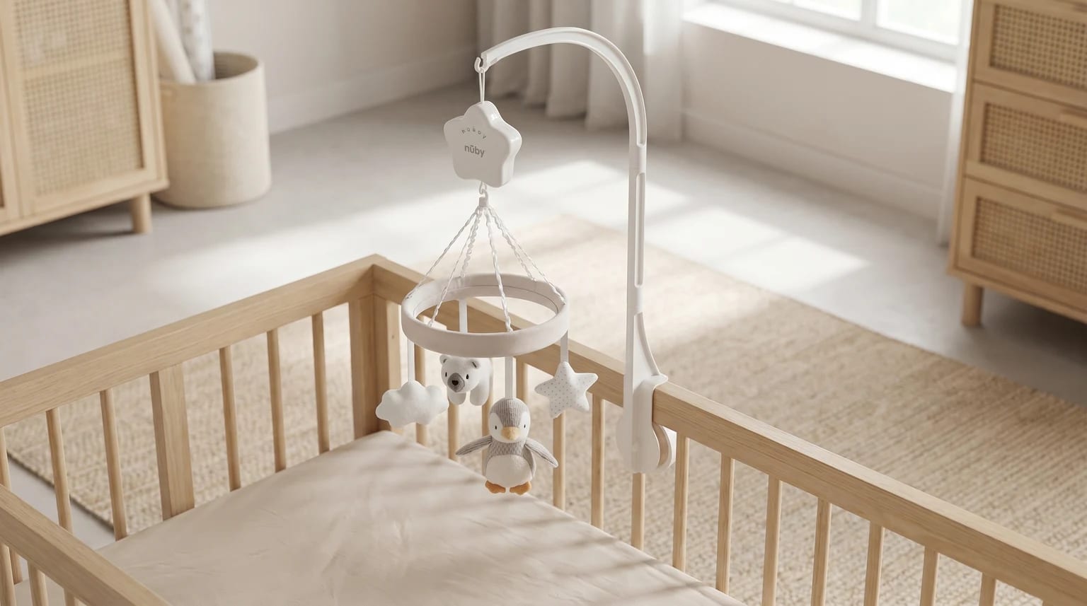 A Nuby musical cot mobile with penguin, polar bear, cloud and star toys securely clamped to a light wood cot in a neutral nursery.