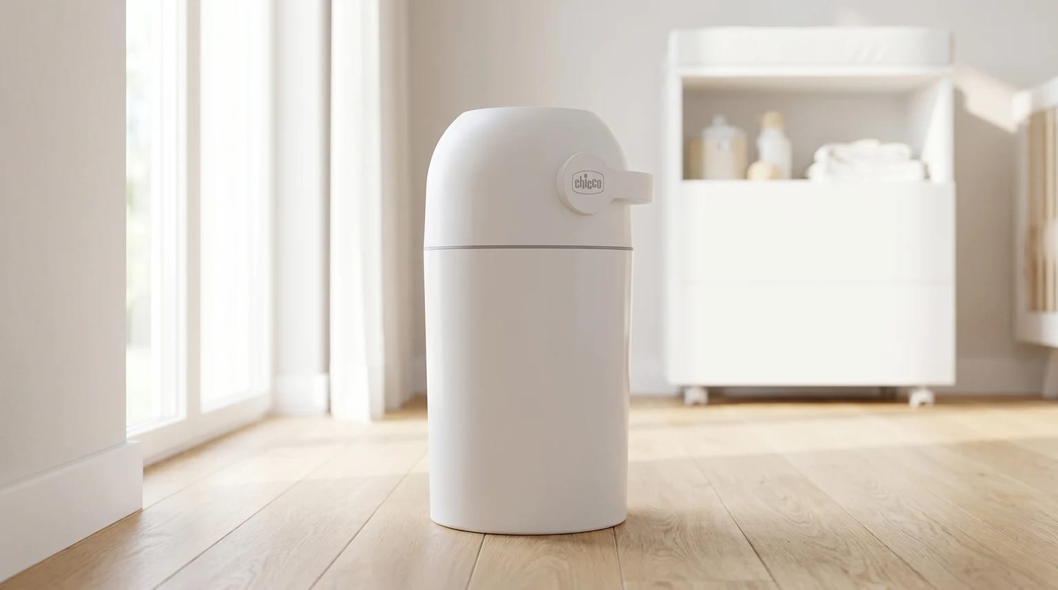 A white Chicco nappy bin standing on a wooden floor in a brightly lit nursery, with a changing table blurred in the background.