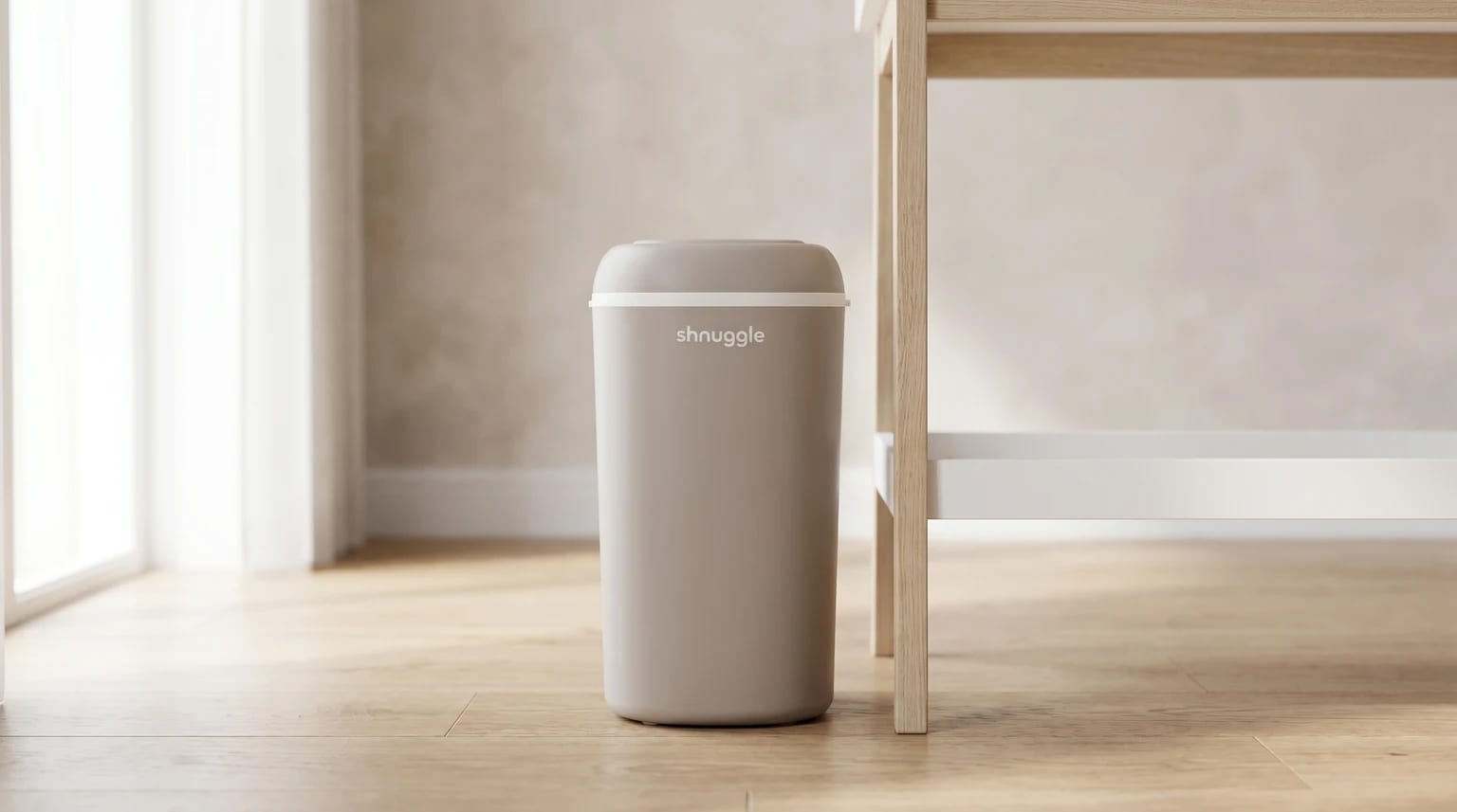 The taupe Shnuggle nappy bin standing on a light wooden floor beside a wood-and-white changing table.