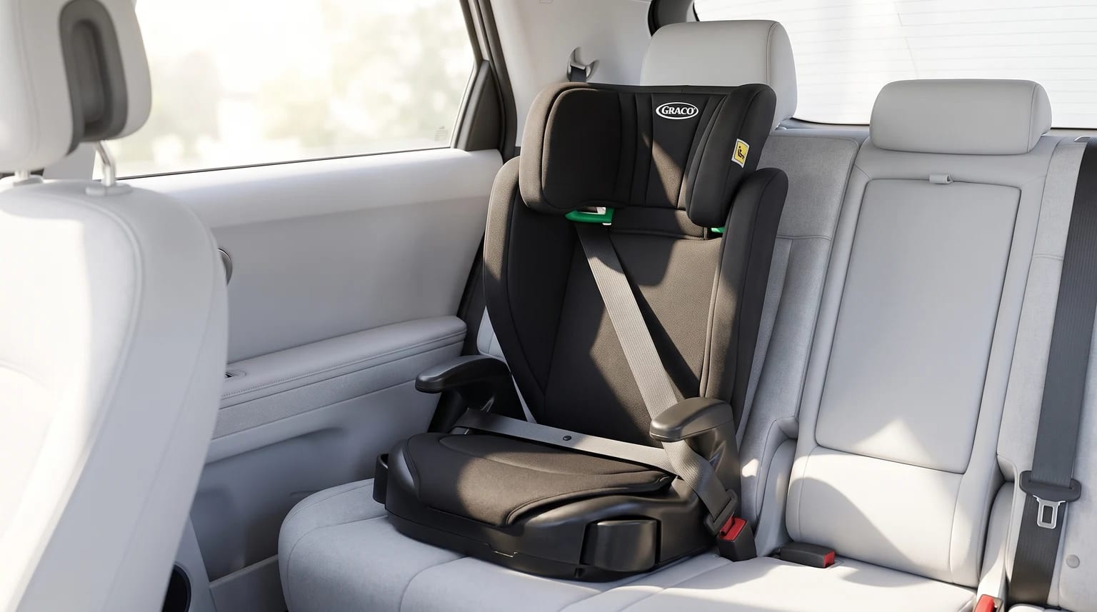 A black Graco high-back booster seat securely installed on a light grey passenger seat in the back of a car.