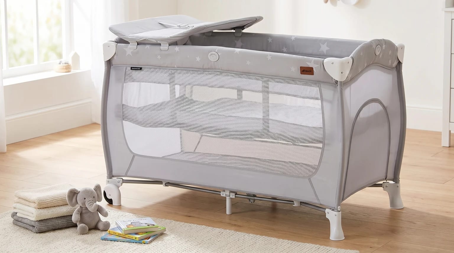 A light grey Hauck Sleep N Play Center travel cot with changing station set up empty in a bright nursery.