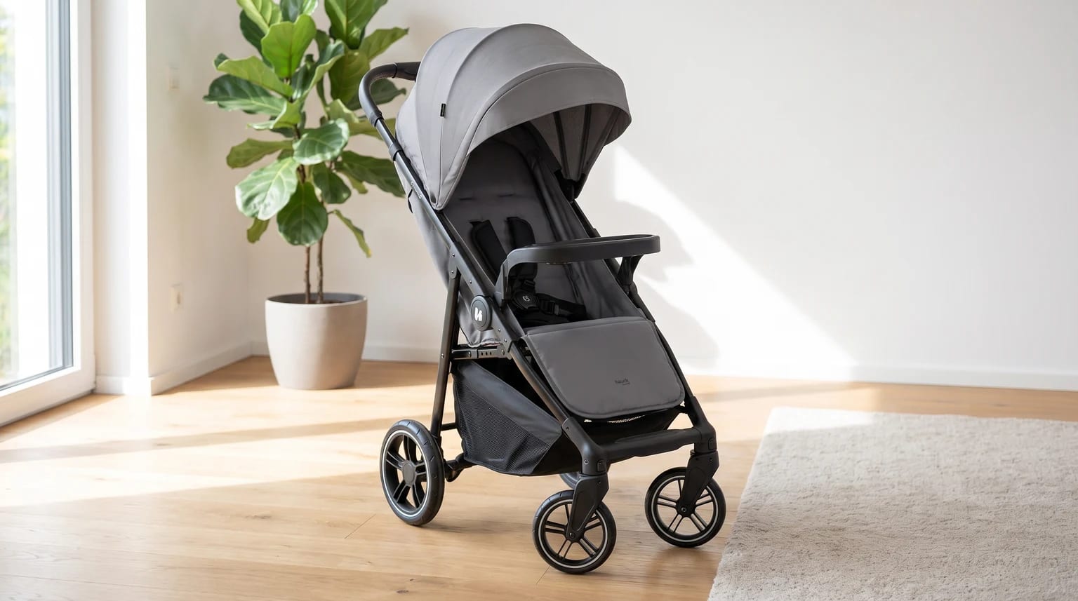 A stylish grey pushchair with a black frame and large sun canopy, pictured in a bright room with a wooden floor.