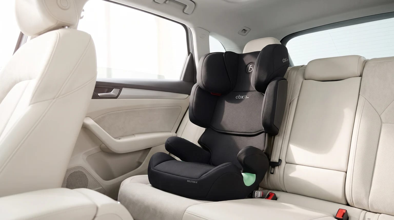 A black CBX high-back booster seat fitted on the cream leather back seat of a car.