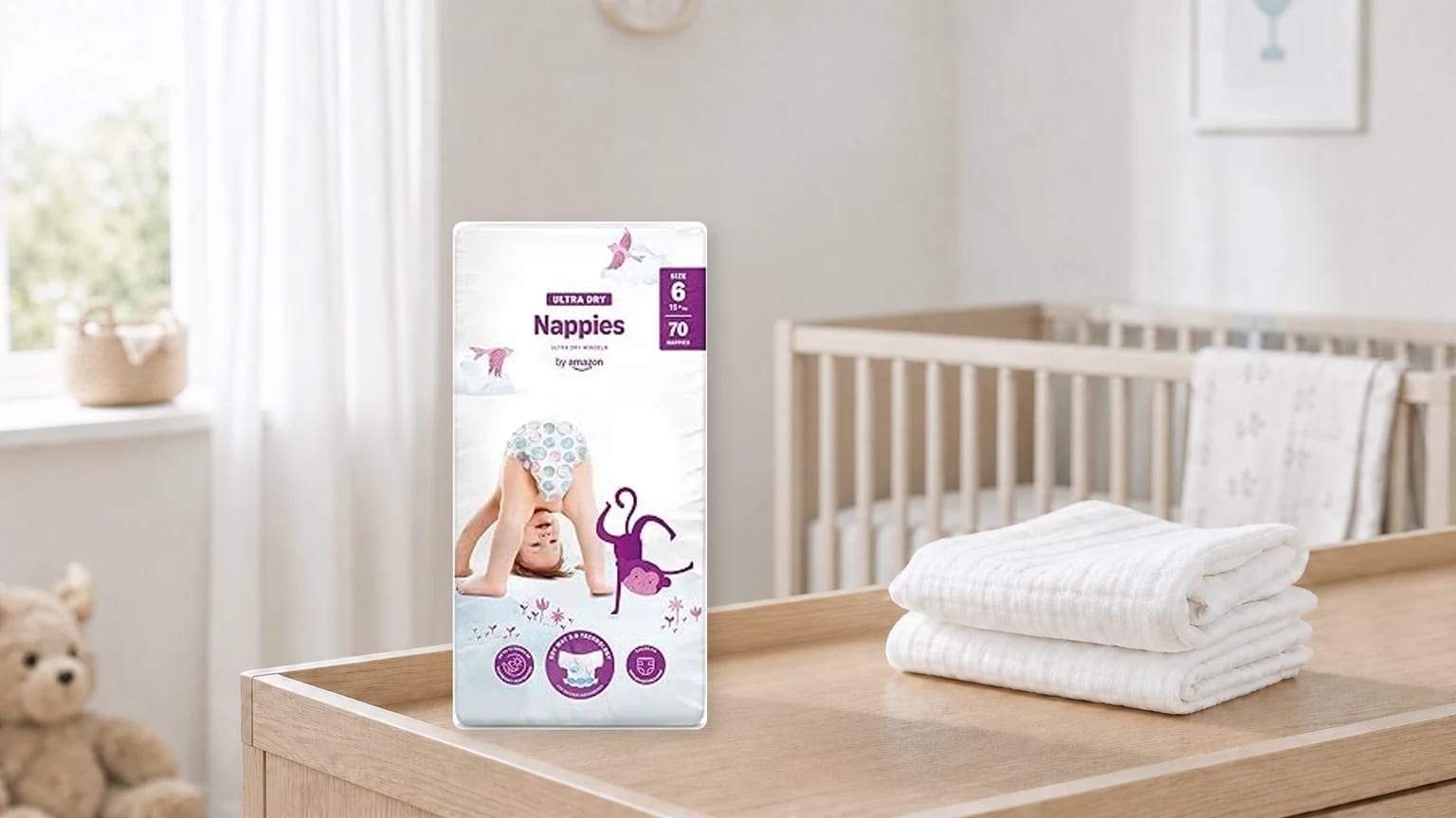 A packet of by Amazon Ultra Dry nappies standing on a wooden changing table in a nursery, next to a stack of white cloths.