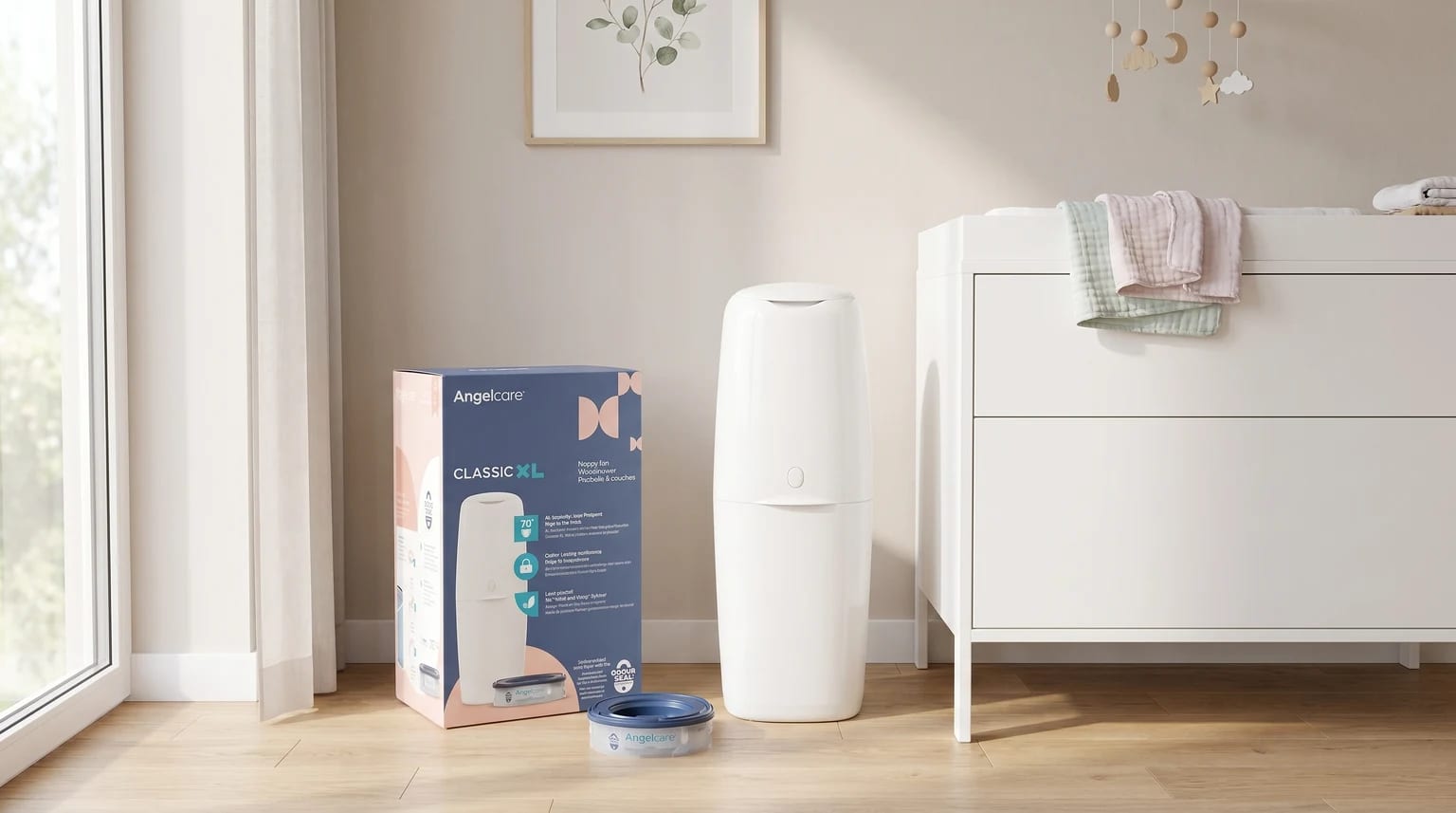 The white Angelcare nappy bin with its box and a refill cassette, placed on the wooden floor of a bright nursery next to a changing unit.