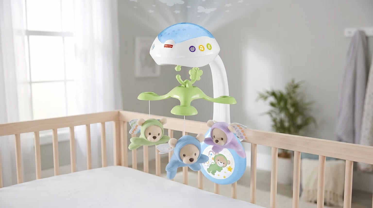 A Fisher-Price projection cot mobile with three soft, winged bear toys in pastel colours, attached to a wooden cot in a nursery.