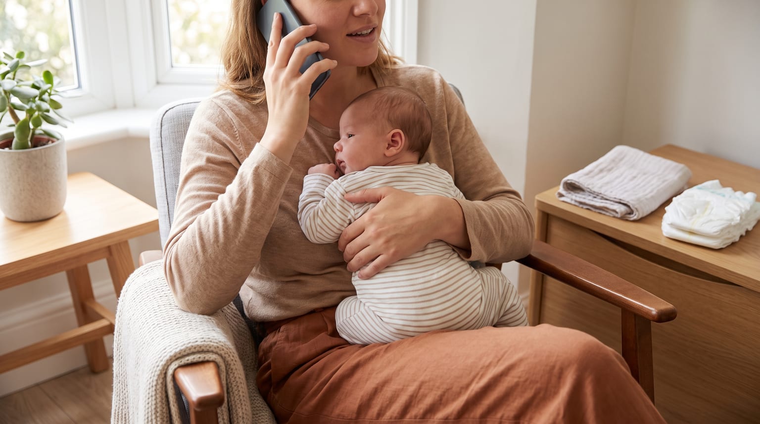 A parent holding a fully clothed baby while making a phone call at home.