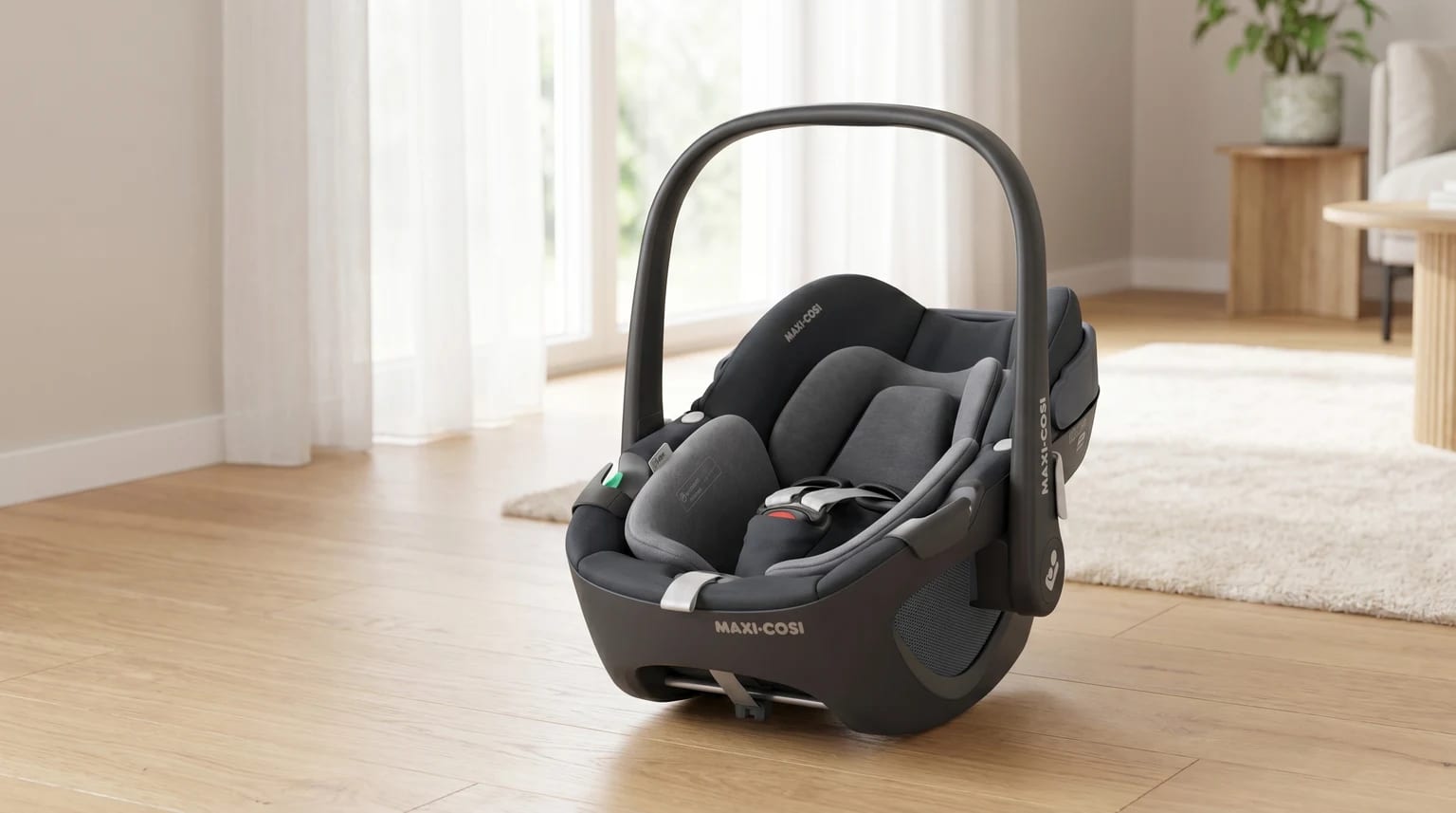 A dark grey Maxi-Cosi infant carrier resting on a light wooden floor in a sunlit living room.