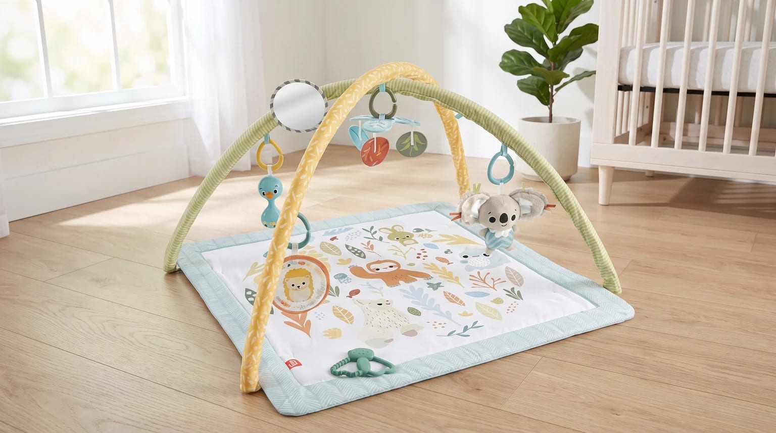 An animal-themed baby play gym with hanging toys, including a koala and a mirror, set up on a wooden floor in a nursery next to a cot.