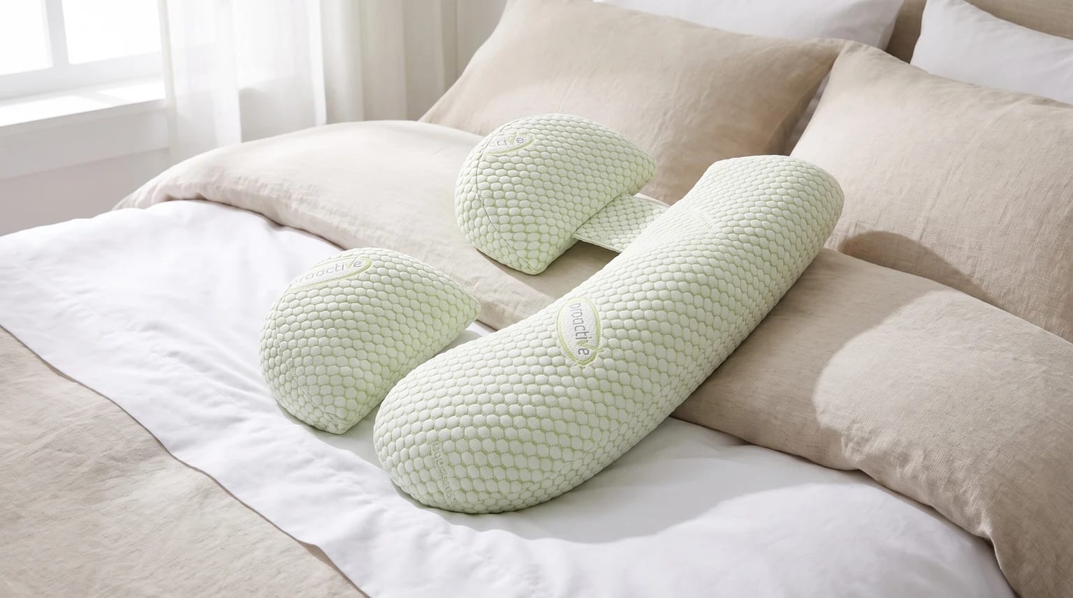 A set of three light green pregnancy support pillows with a honeycomb texture, laid out on a bed with white and beige linen.