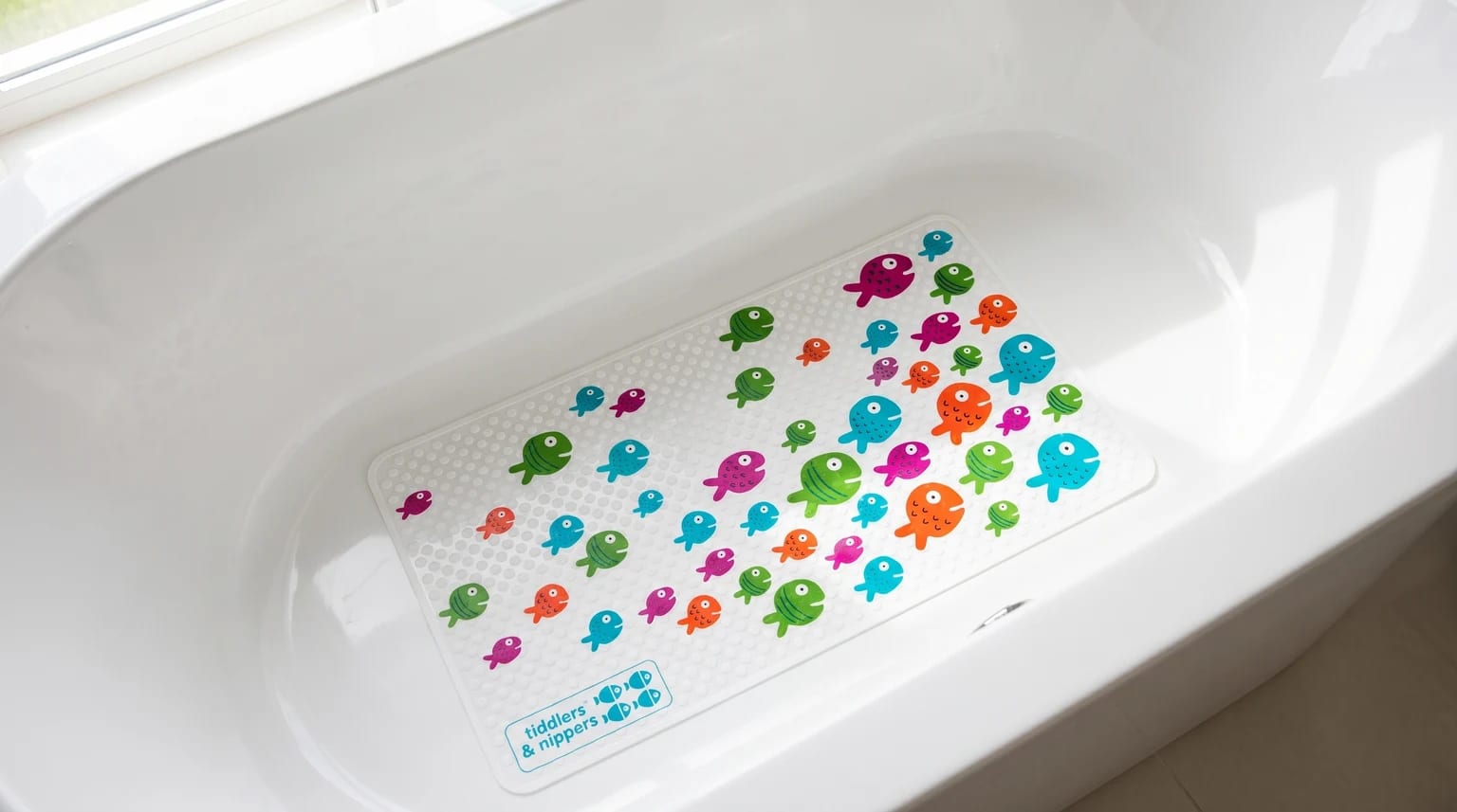 A non-slip bath mat with a colourful pattern of cartoon fish sits at the bottom of a clean white bath.