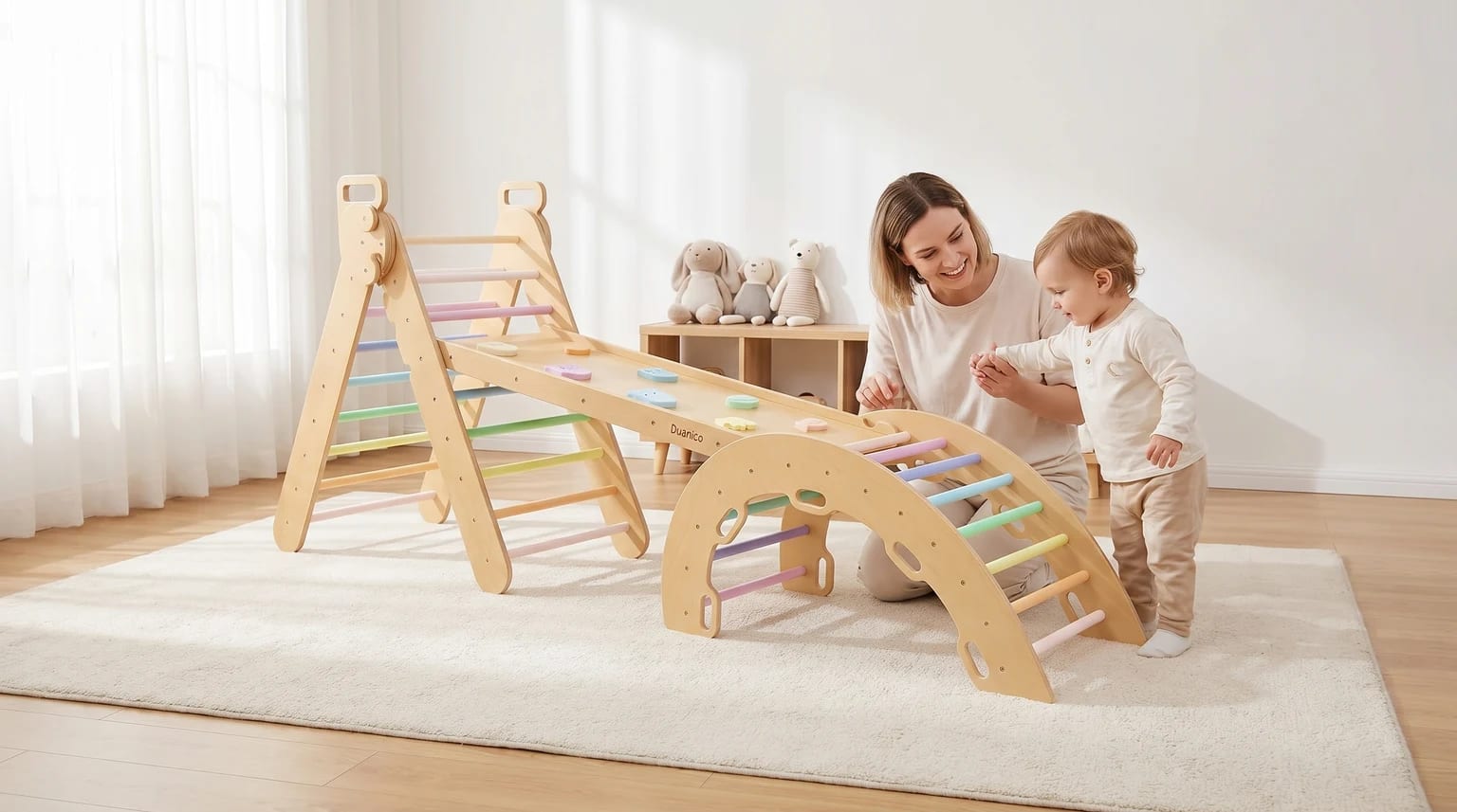 A mother encourages her toddler beside a wooden climbing frame set up with a triangle, arch, and a ramp with pastel-coloured holds.