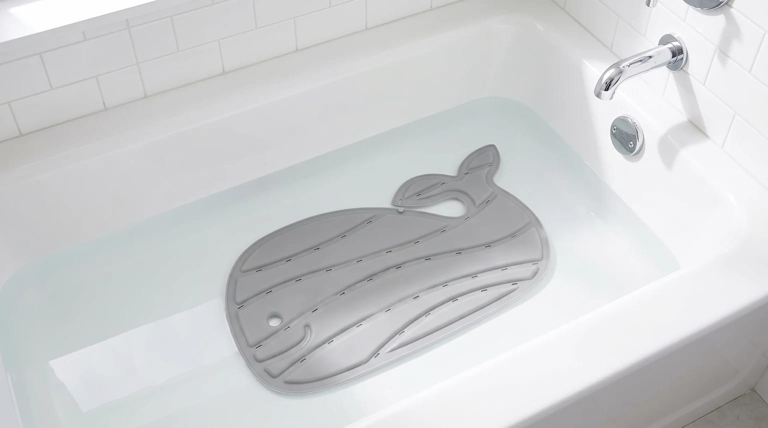A grey, whale-shaped non-slip mat sitting at the bottom of a white bath filled with water.