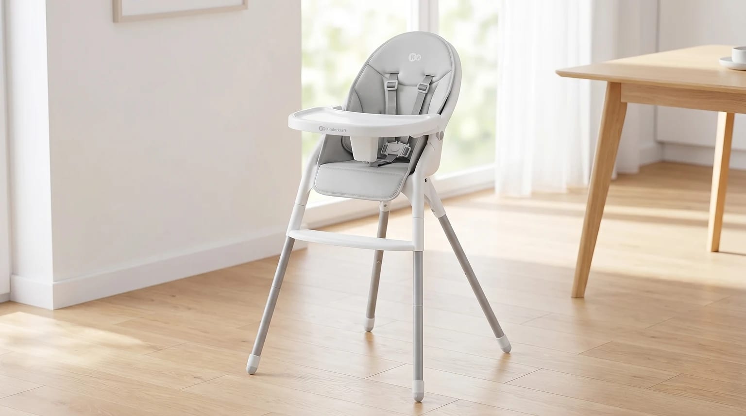 A modern, light grey high chair with a white frame and tray, standing on a wooden floor in a sunlit dining room.