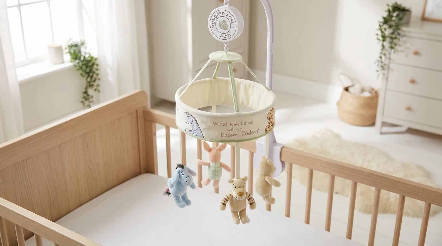A Winnie the Pooh musical cot mobile with Eeyore, Tigger, Piglet, and Pooh plush toys hanging over a light wood cot in a softly lit baby's room.