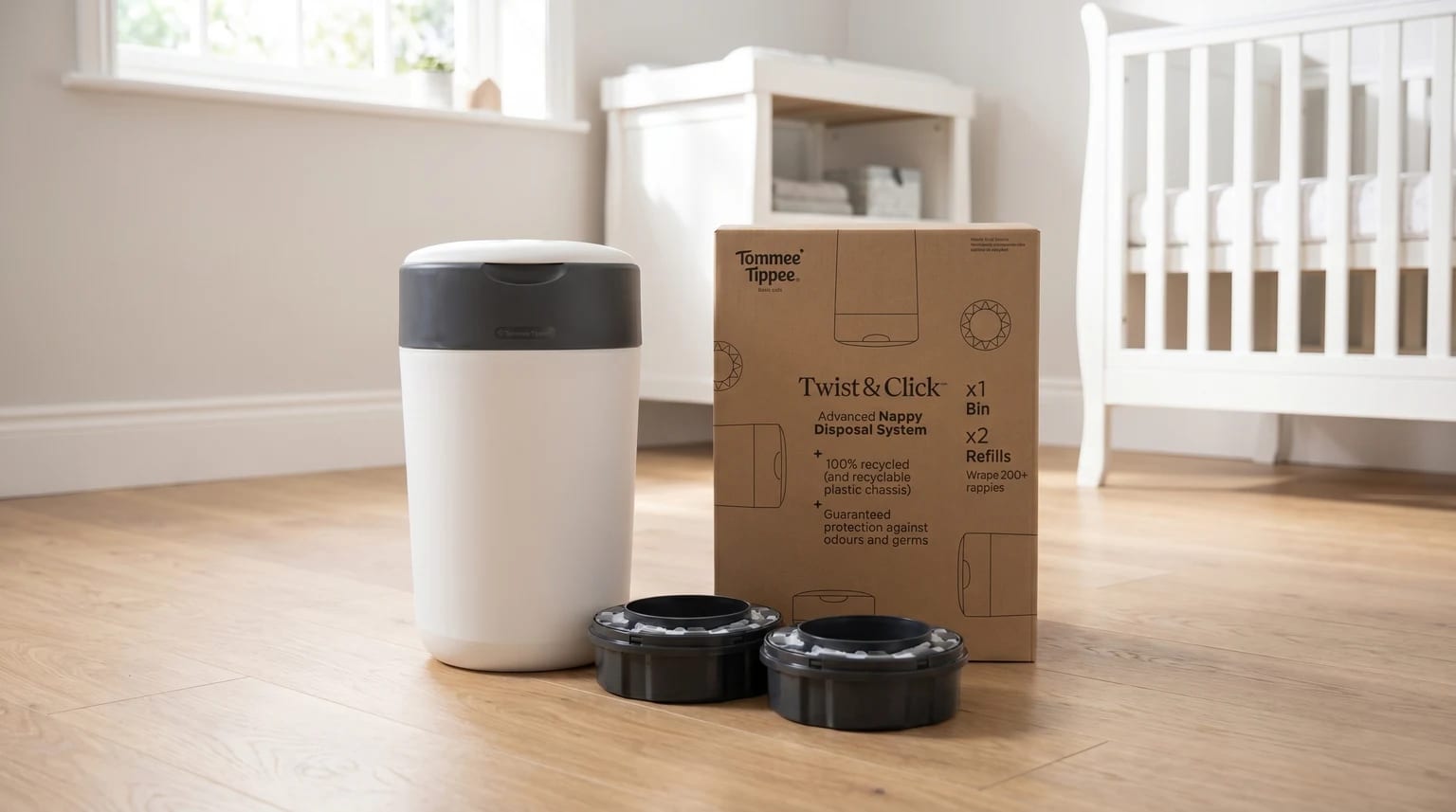 A Tommee Tippee nappy bin with its box and two refill cartridges, shown on the wooden floor of a bright nursery with a cot in the background.